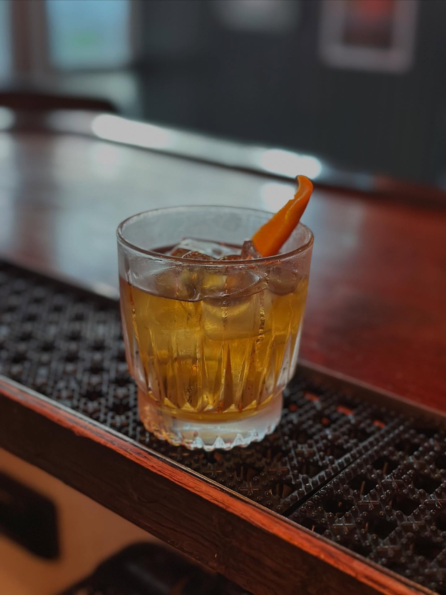 Glass of amber liquid with ice, orange peel on a bar.