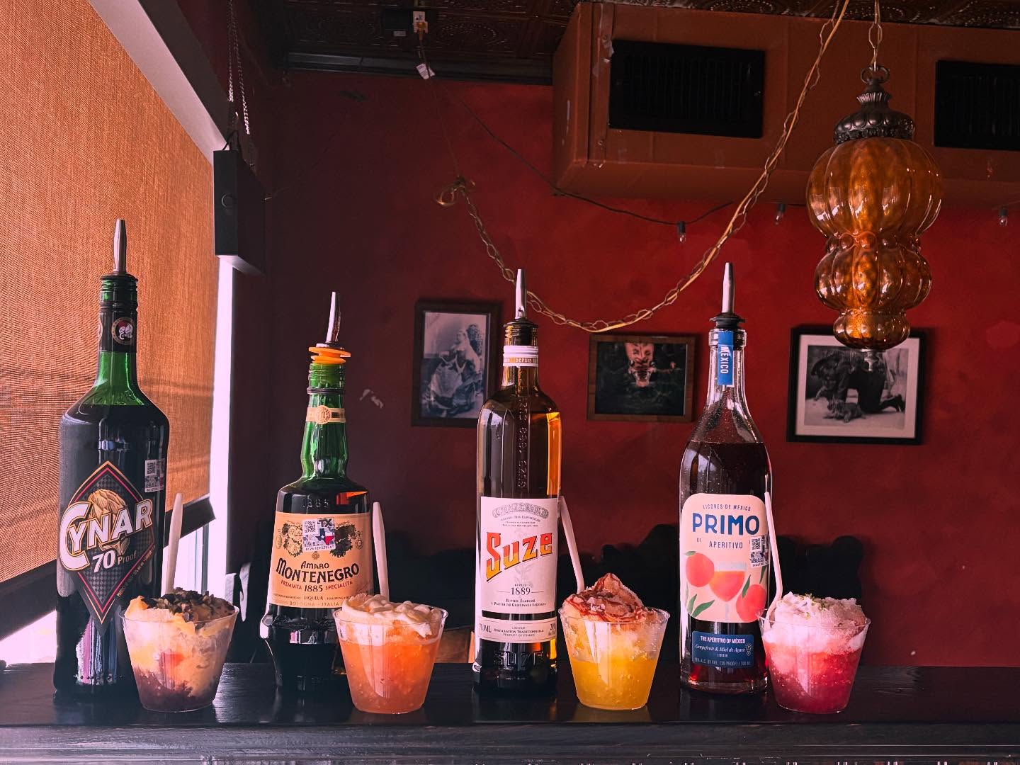 Four aperitif bottles with colorful shaved ice drinks on a bar.