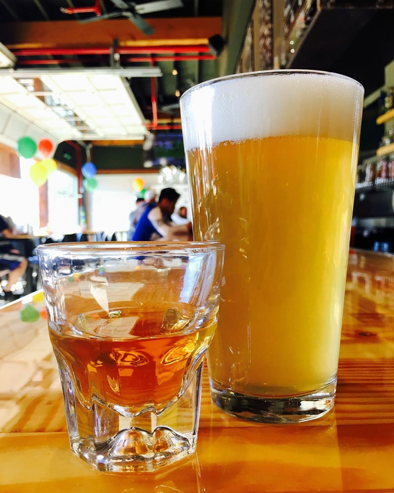 Frothy beer and a shot on a wooden bar table.