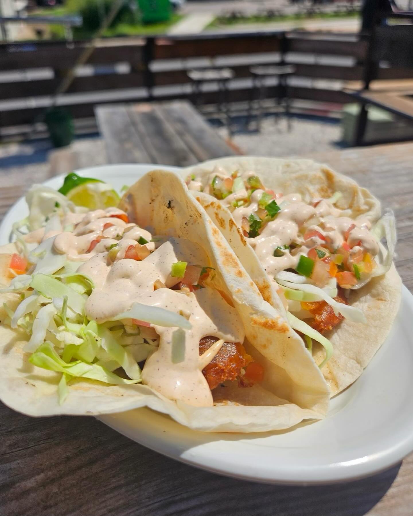 Two tacos topped with lettuce, diced vegetables, sauce, and lime.