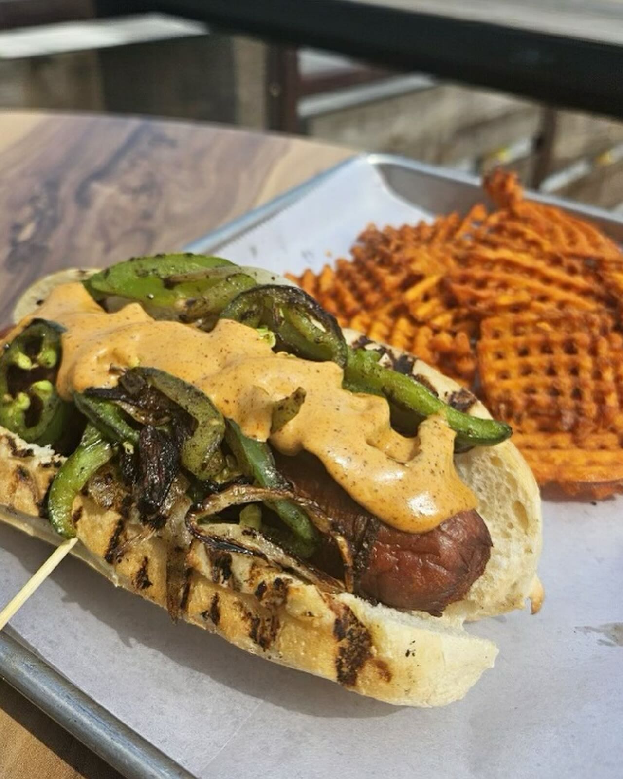 Hot dog with grilled peppers, creamy sauce, and sweet potato waffle fries.