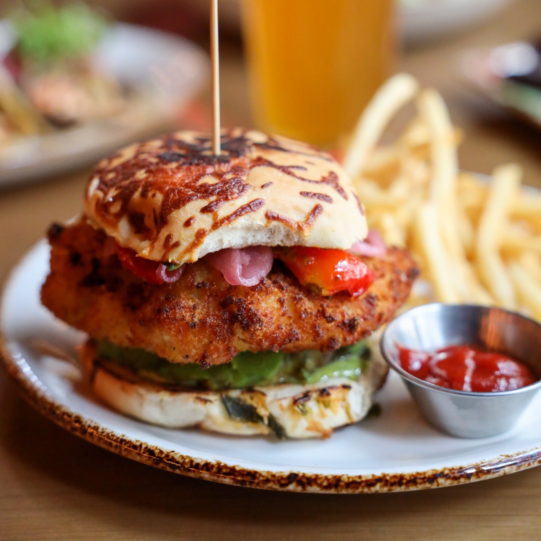 Fried chicken sandwich with guacamole, onion, tomato, fries, ketchup.