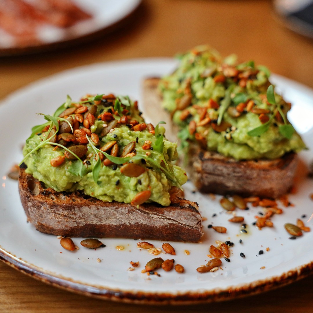 Avocado toast with pumpkin seeds and fresh greens on a plate.