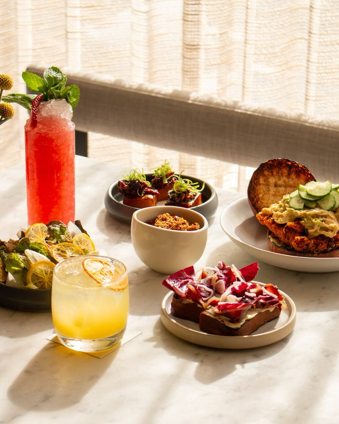 A sunny table with cocktails, appetizers, and several food dishes.