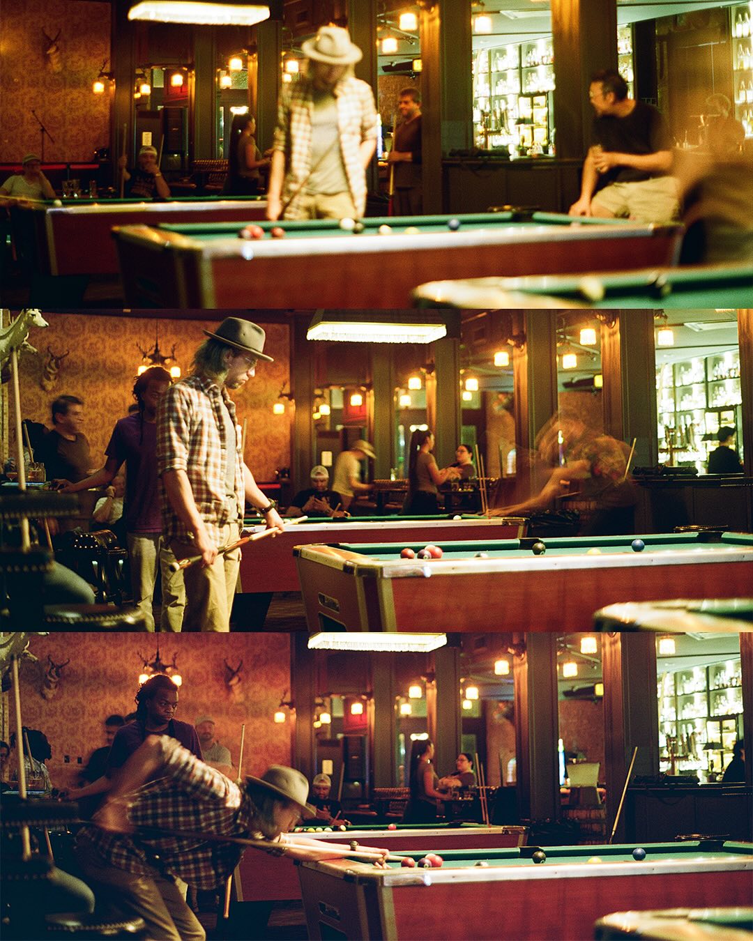 People playing billiards in a warmly lit, crowded pool hall.
