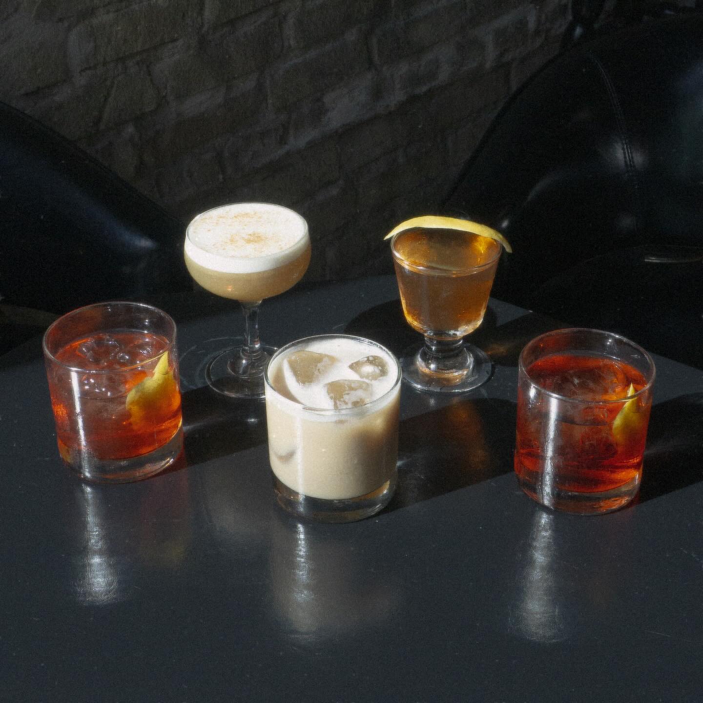Five assorted cocktails with ice and garnishes on a dark table.