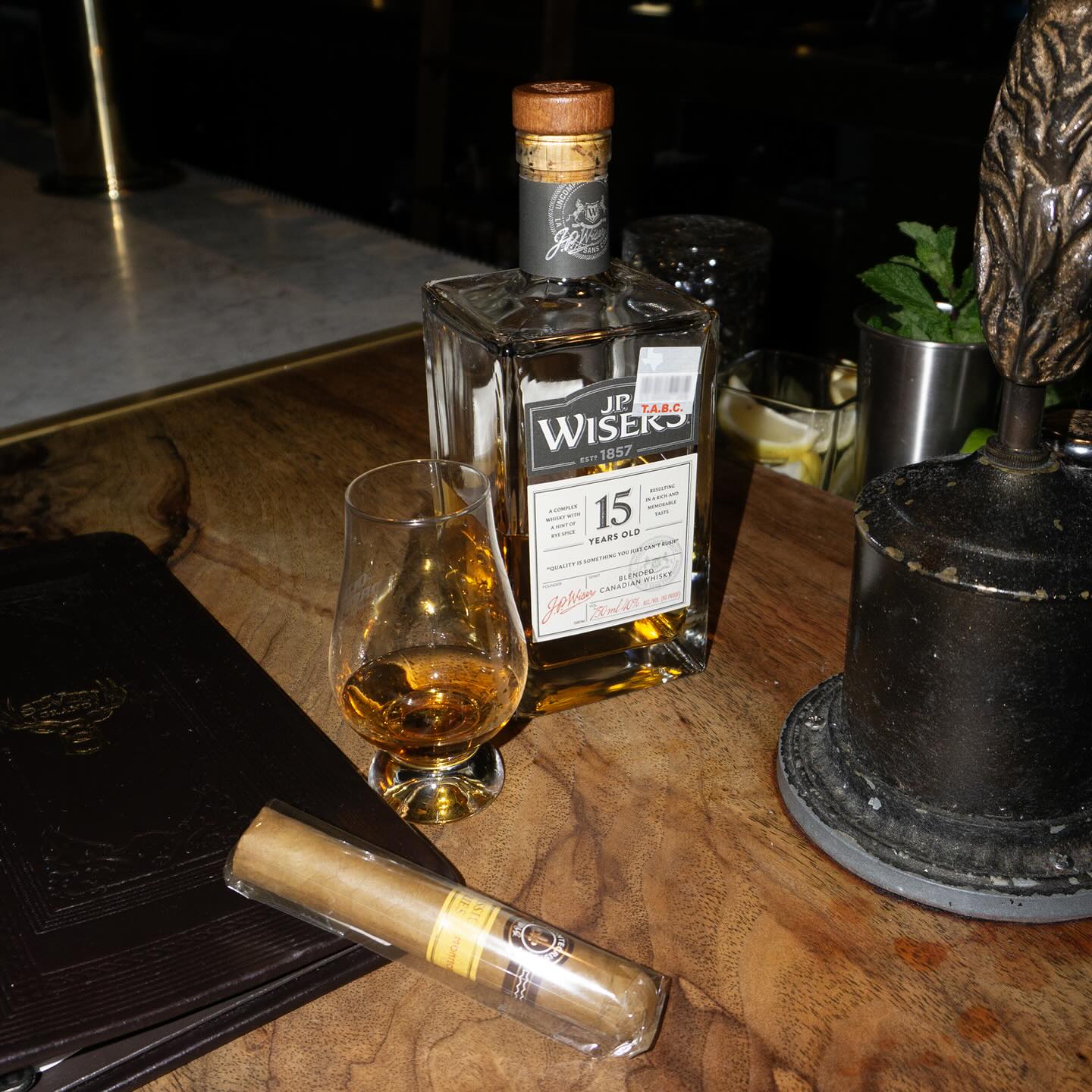 JP Wiser's 15-year-old whisky, glass, and cigar on a table.