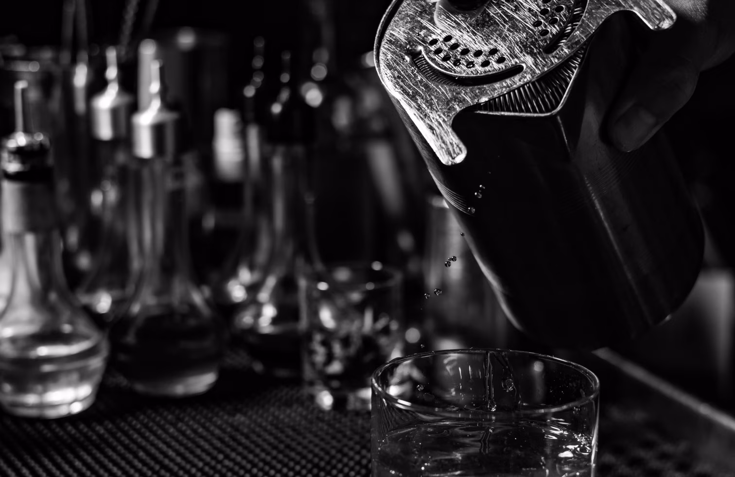 Bartender pouring a drink from a shaker into a glass.