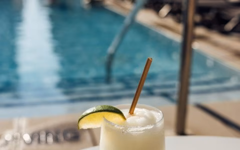 Frozen drink with lime and straw by a swimming pool.