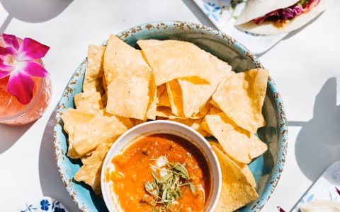 Tortilla chips and salsa with a pink drink and orchid.