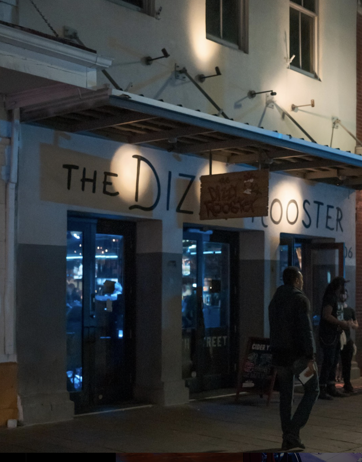 Night shot of The Dizzy Rooster bar entrance with people outside.