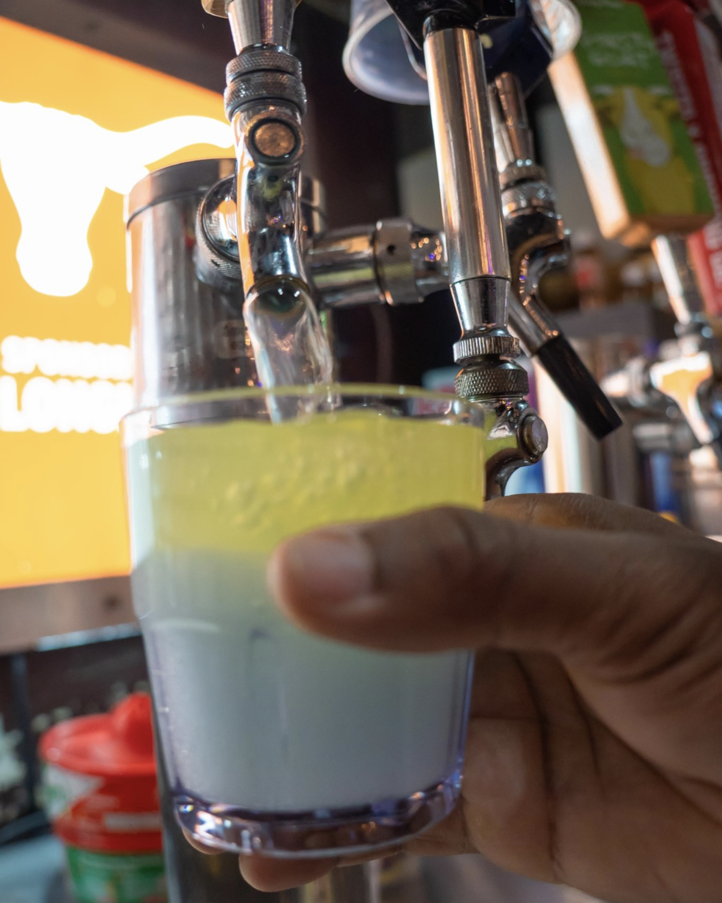 Hand holds cup as yellow liquid pours from a beverage tap.