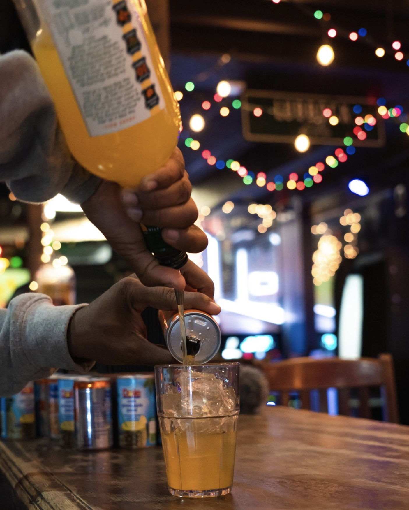 Hands pouring orange drink from can into iced glass.