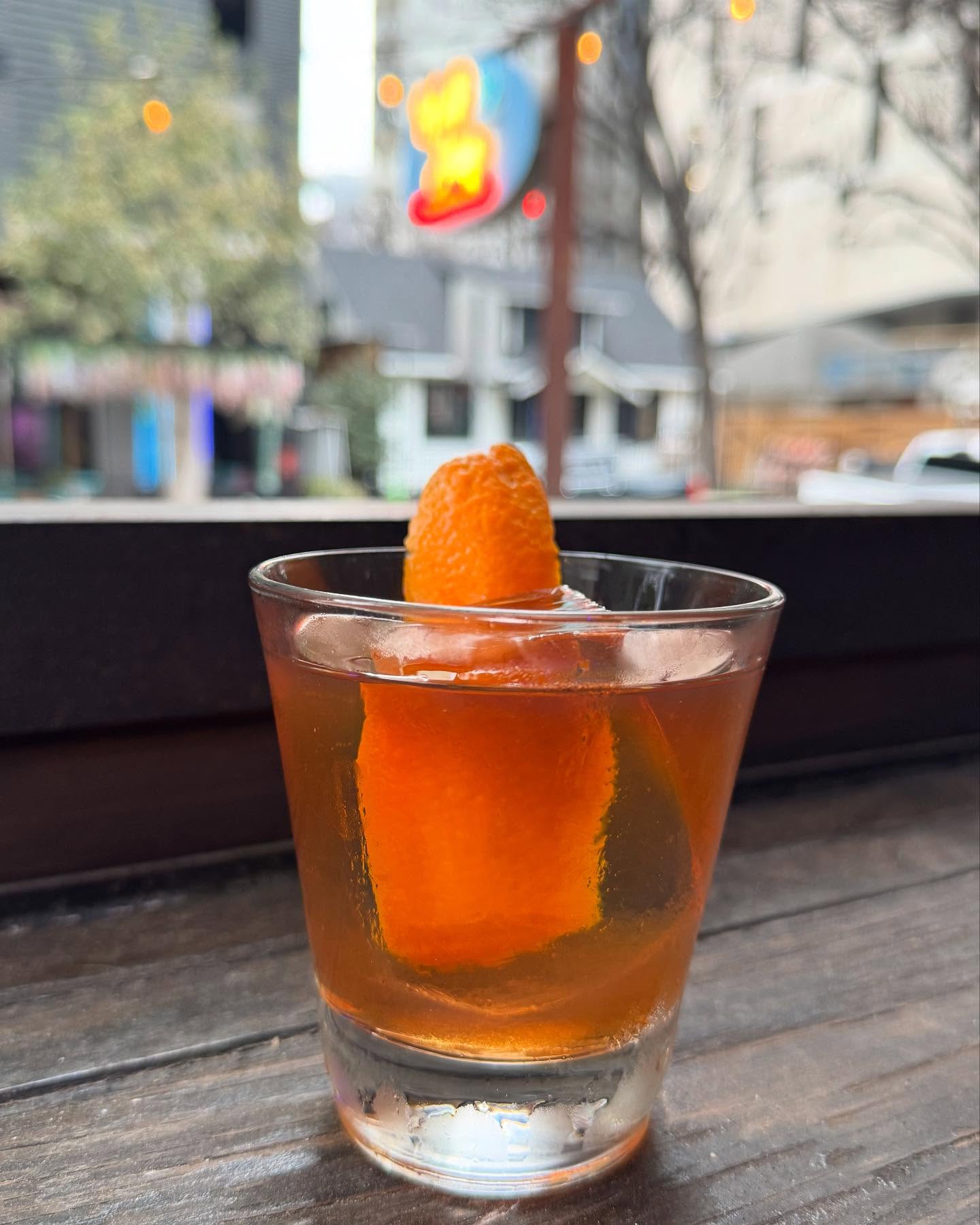 Amber drink with large orange peel and ice on wood.