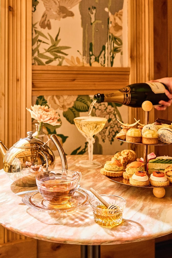 Hand pouring champagne into a glass, next to tea and pastries.