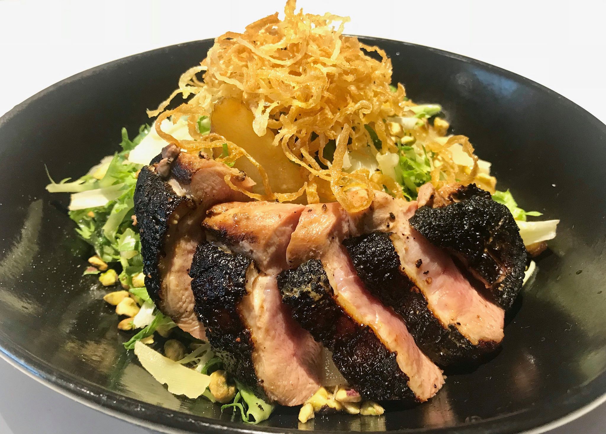 Sliced seared meat, salad, pistachios, and crispy fried onions.