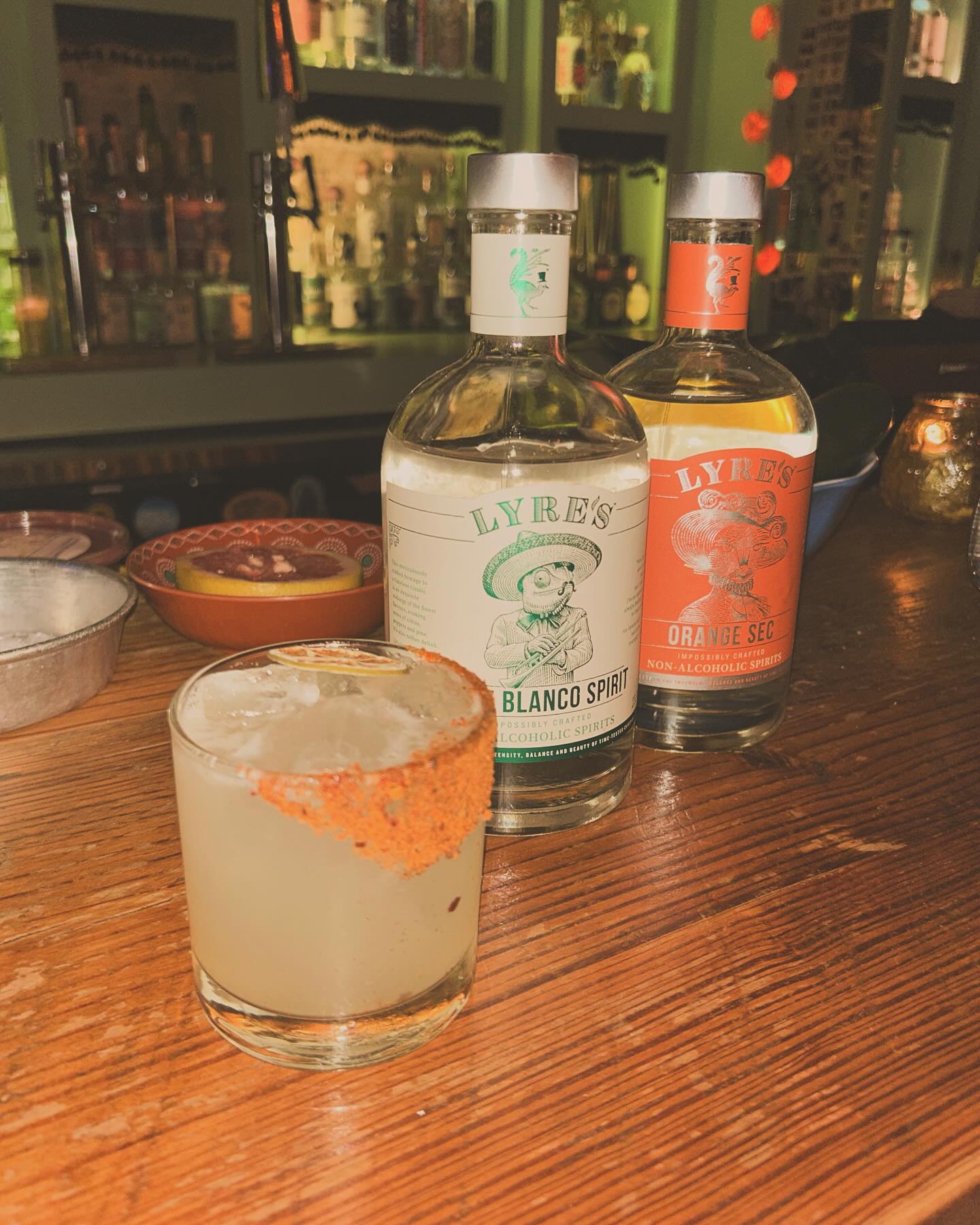Spiced-rim cocktail and two Lyre's non-alcoholic spirits on a bar.