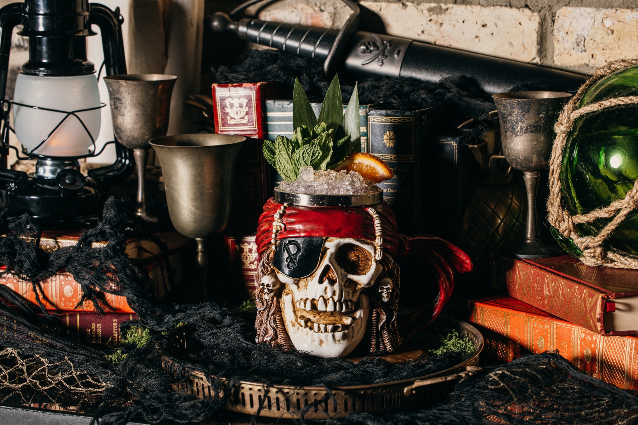 Pirate skull mug drink surrounded by old books, lantern, and sword.