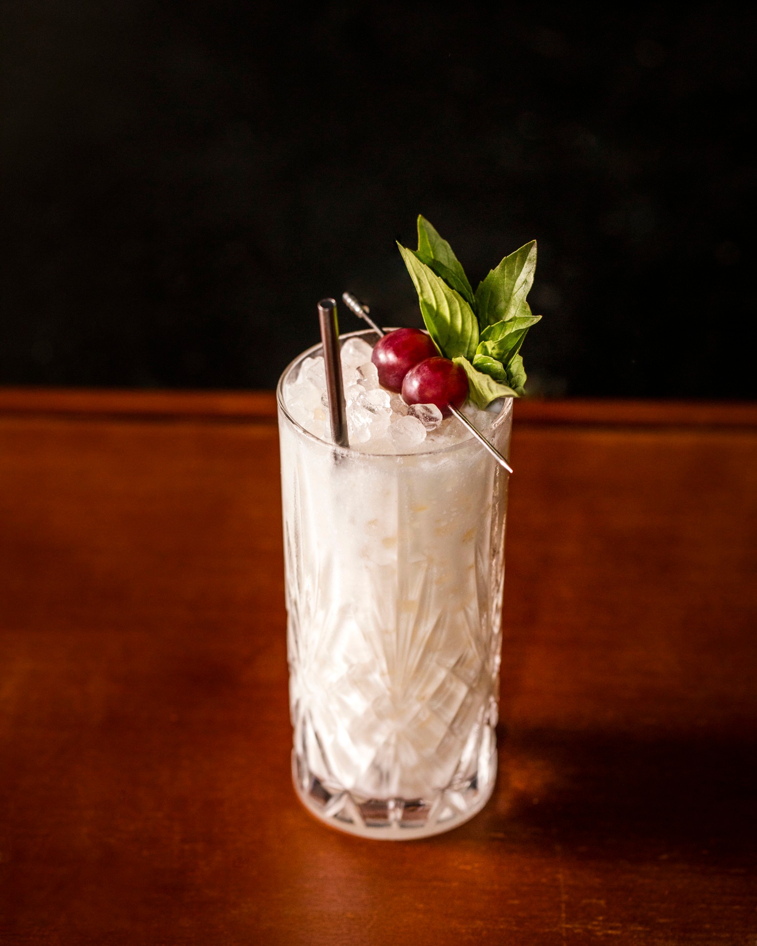 Tall glass with icy white drink, cherries, basil, and a straw.