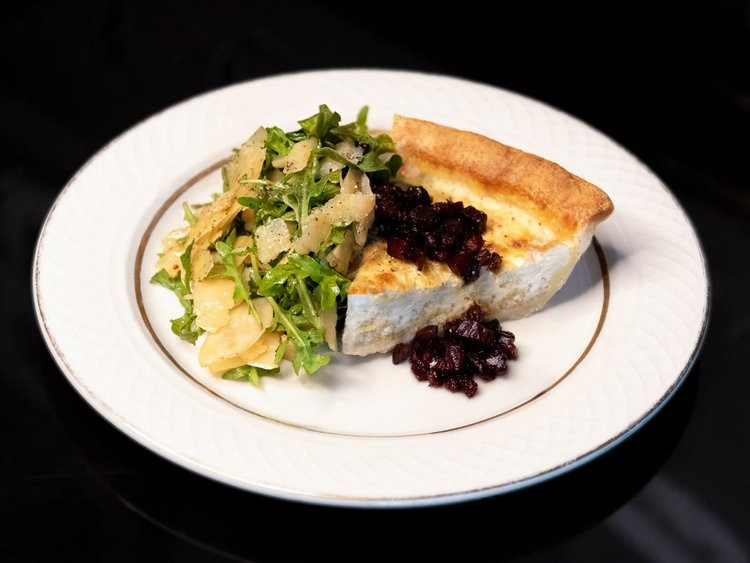 Slice of quiche with green salad and dark red topping.