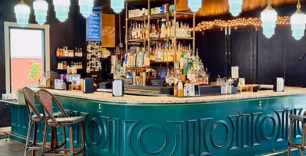 Bar interior with green counter, liquor bottles, beer taps, and stools.