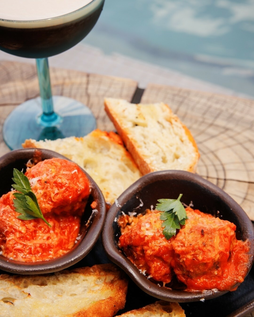 Two bowls of meatballs with bread and a cocktail.