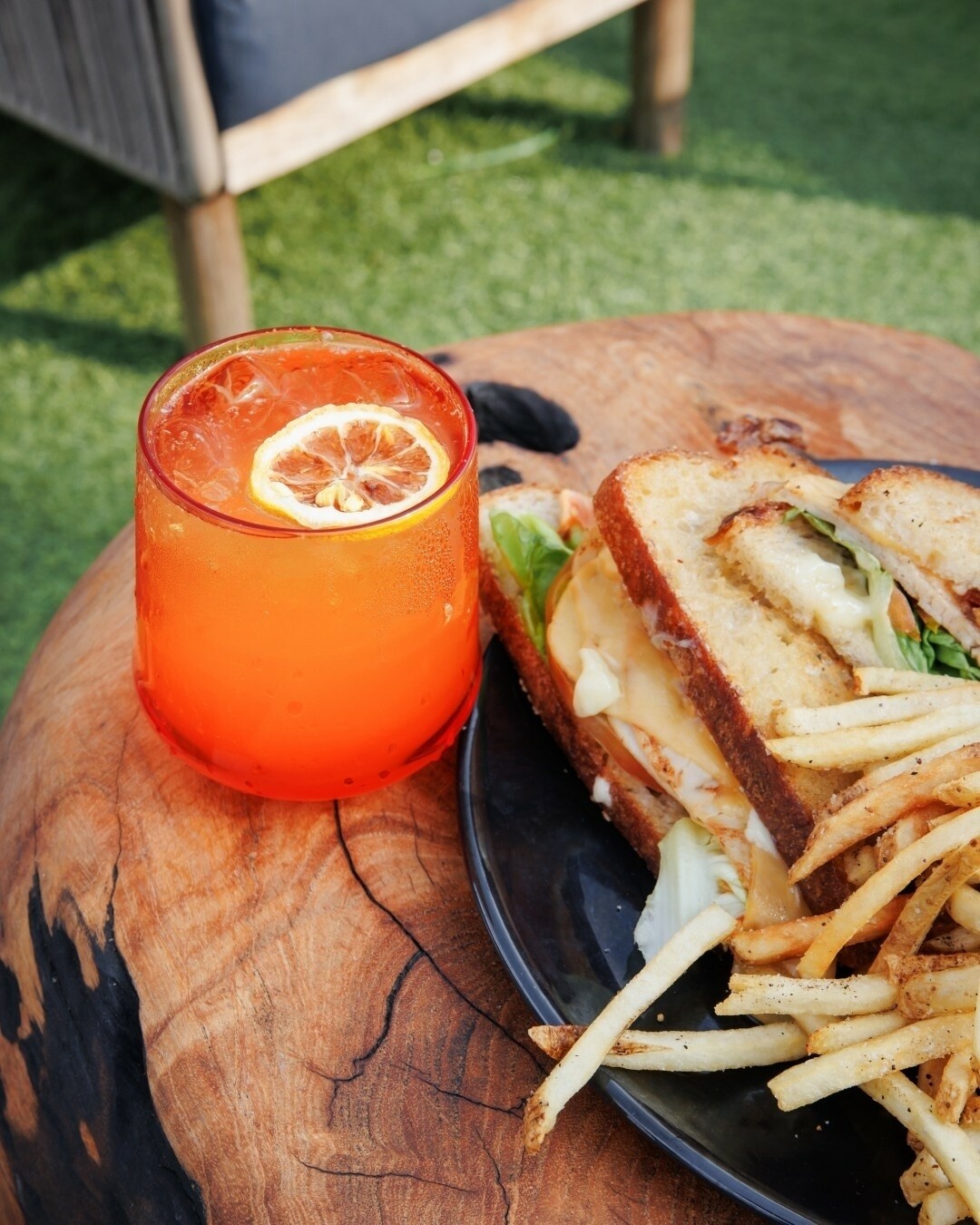 Orange drink with lemon slice, toasted sandwich, and fries on wood.
