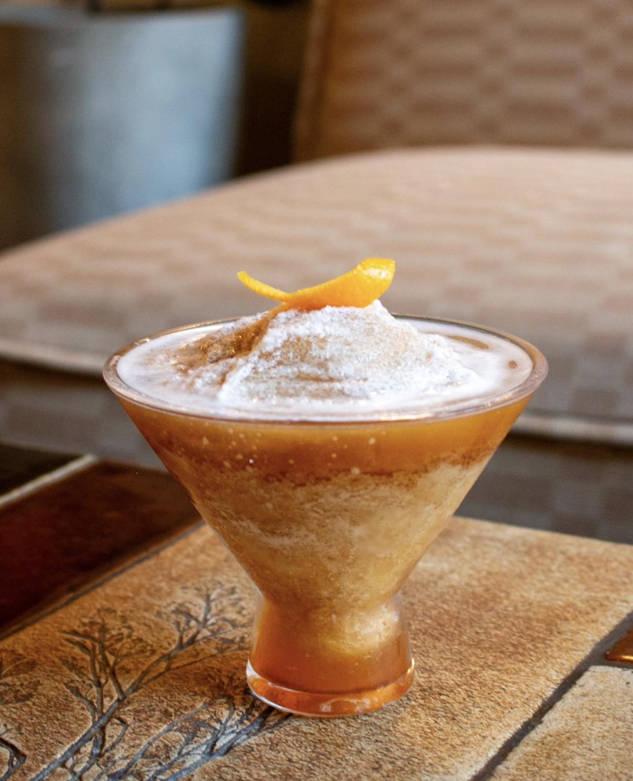 Amber frozen layered drink with orange peel and white powder.