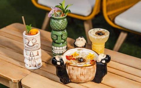 Four decorative tiki cocktails on a wooden outdoor table.