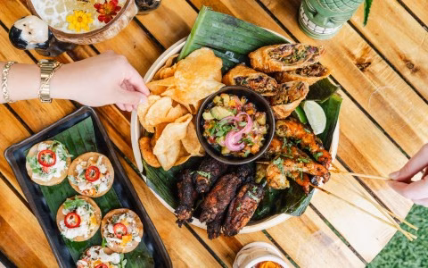 Hands picking chips and skewers from a large appetizer platter.