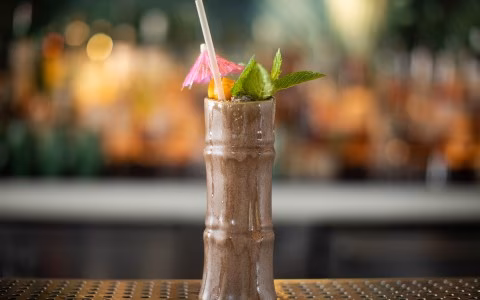 Cocktail in a bamboo-style glass with mint, umbrella, and straw.
