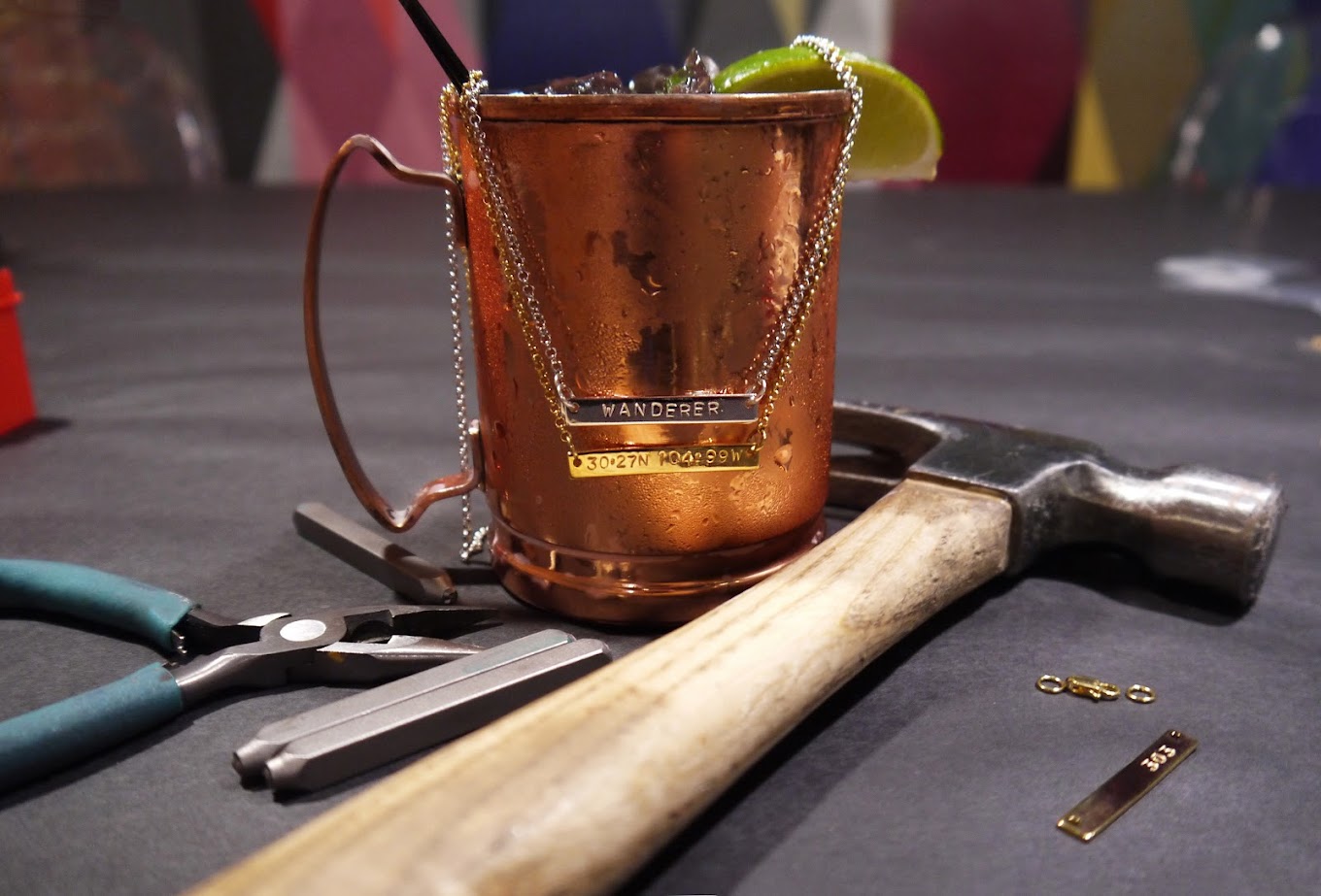Custom "WANDERER" and coordinate necklaces with jewelry tools and a copper mug.