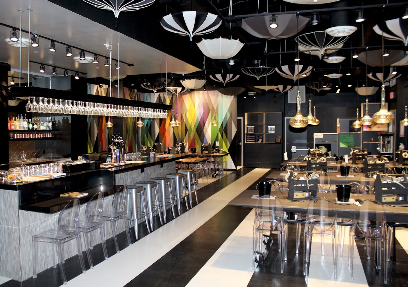 Bar interior with black-and-white umbrellas, geometric wall, and striped floor.