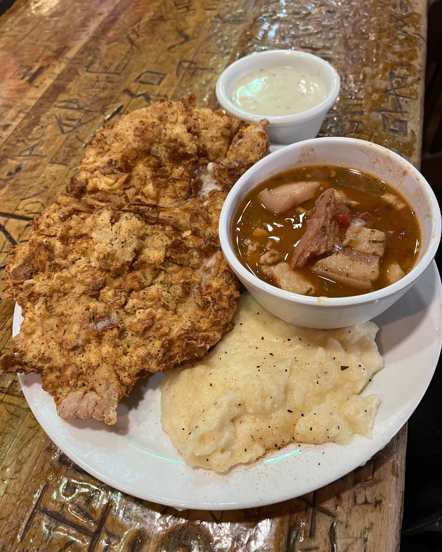 Fried chicken, stew, mashed potatoes, and white sauce on carved wood.