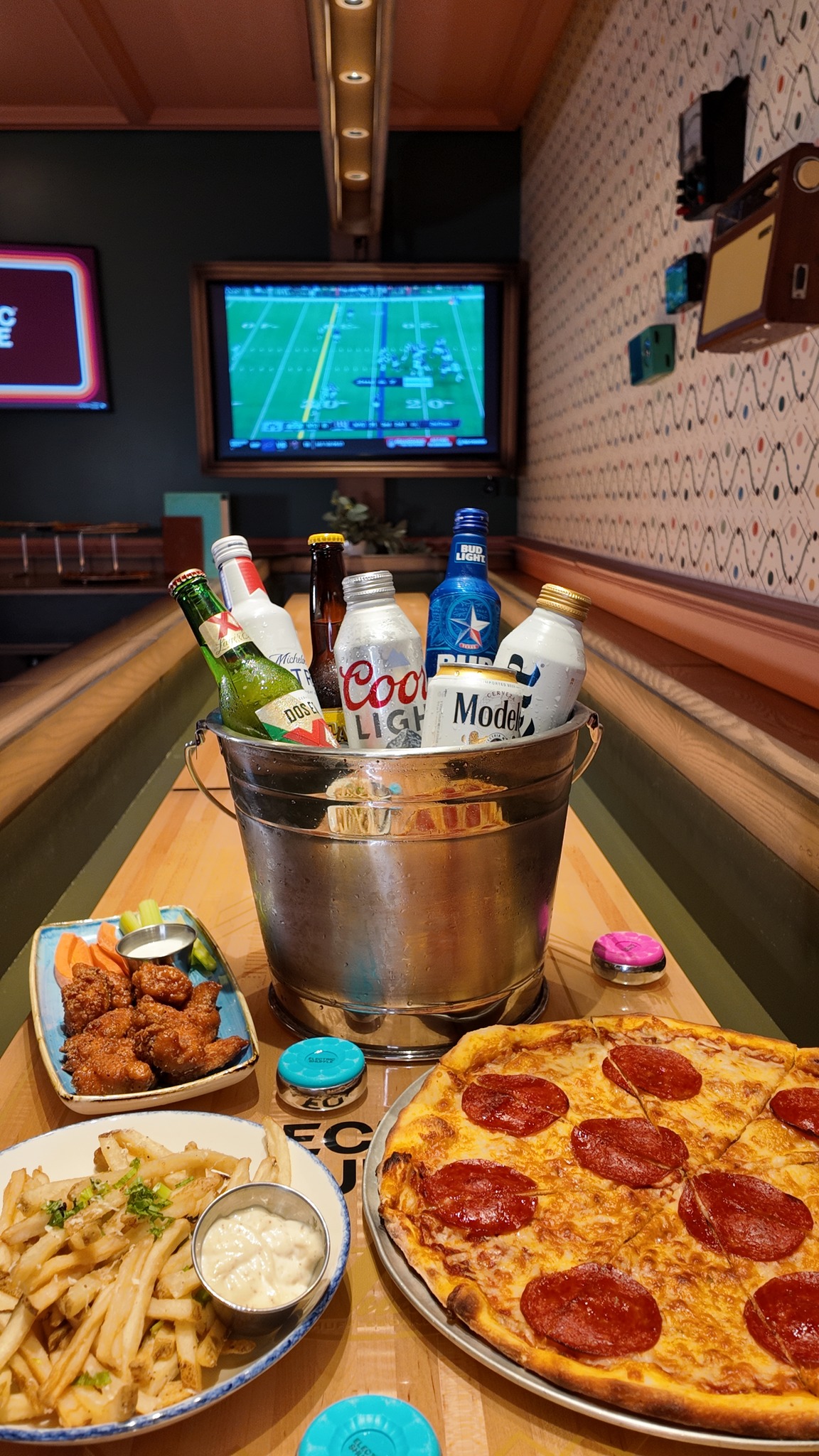 Pepperoni pizza, wings, fries, and beer bucket with football game.