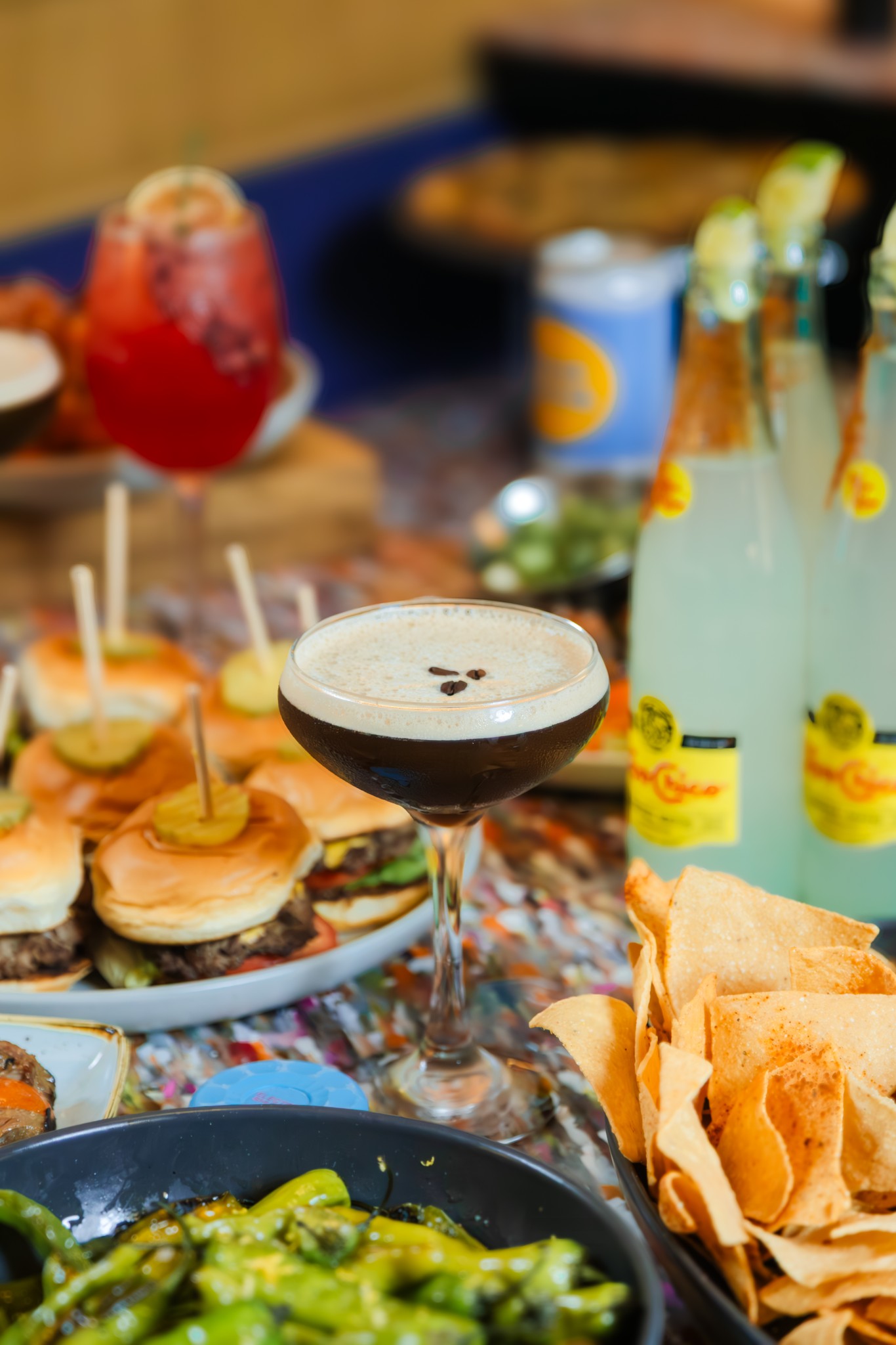 Cocktail with coffee beans, mini burgers, chips, and drinks on a table.