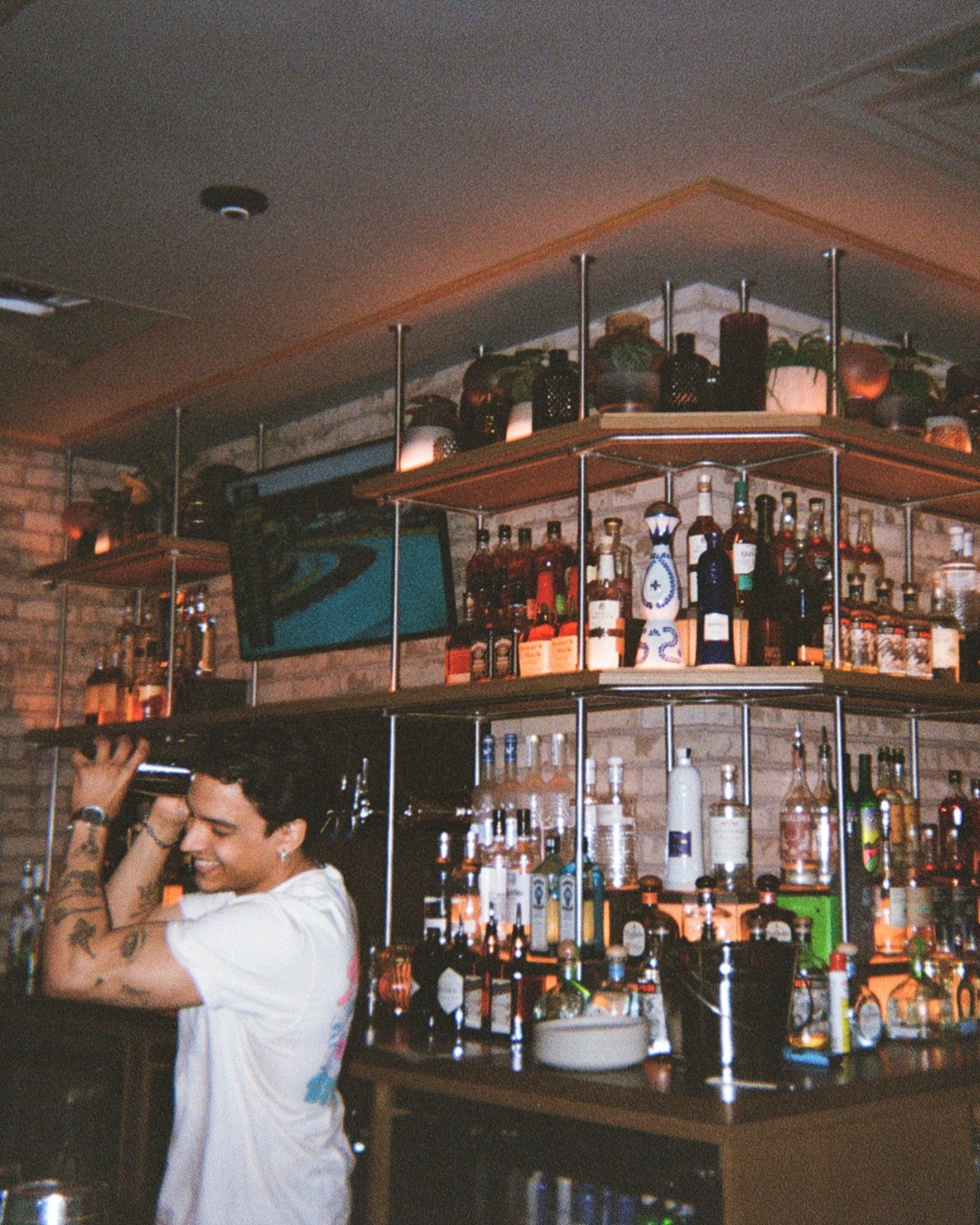 Smiling bartender shaking a drink at a well-stocked bar.