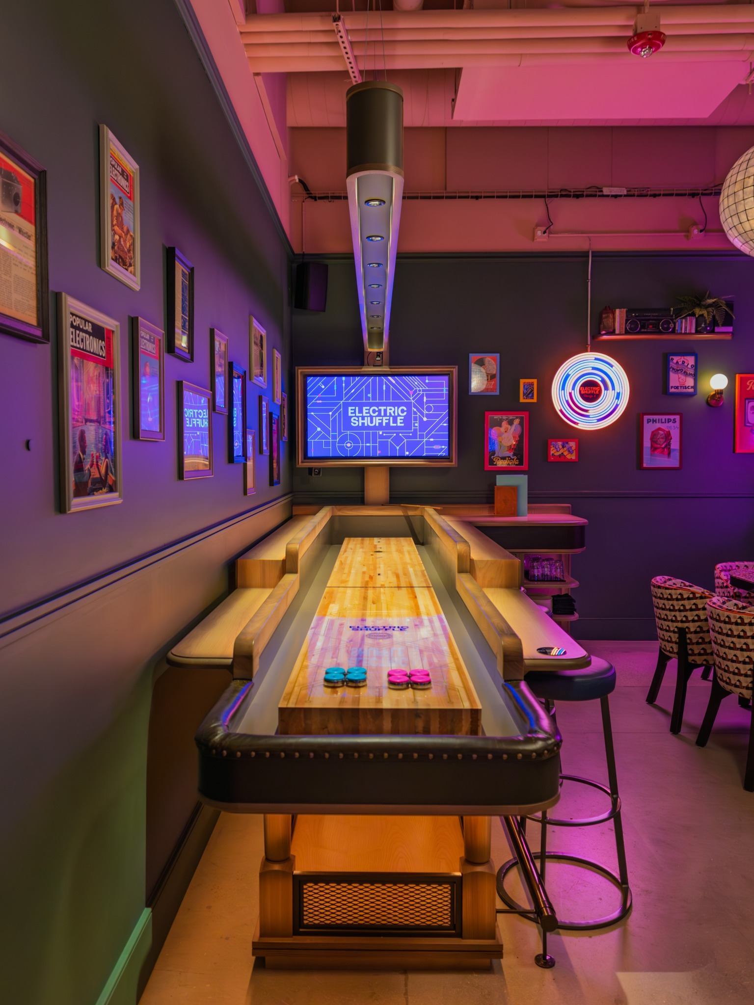 Neon-lit indoor shuffleboard court with "Electric Shuffle" screen.
