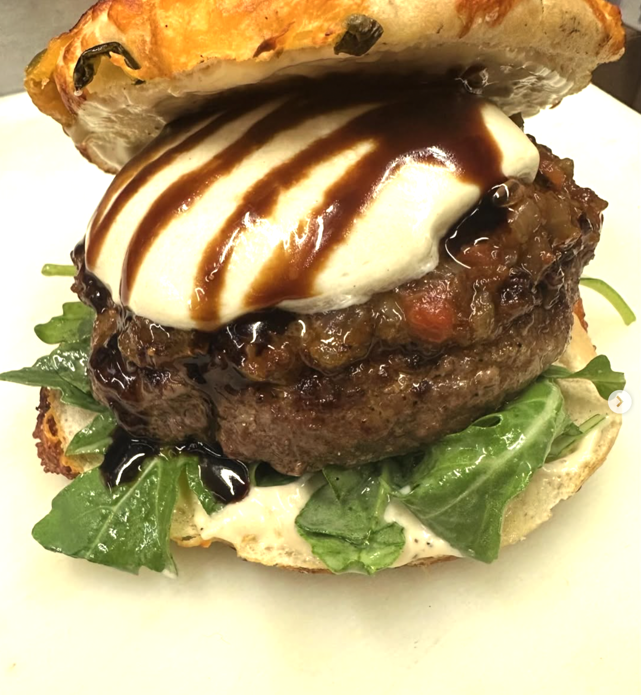 Burger with melted white cheese, dark glaze, relish, and arugula.