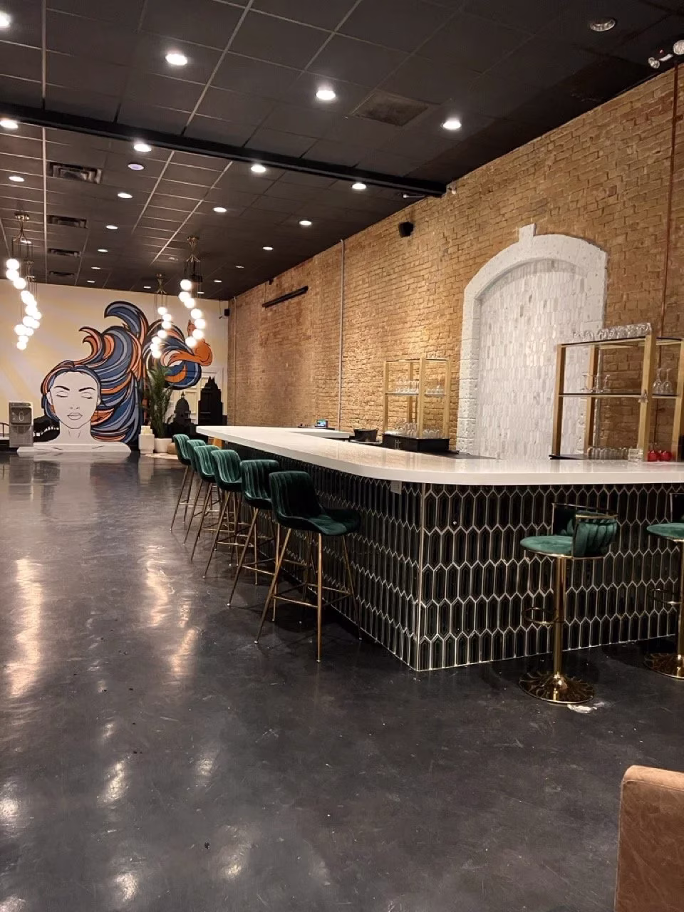 Long bar with green stools, wall mural, and exposed brick.