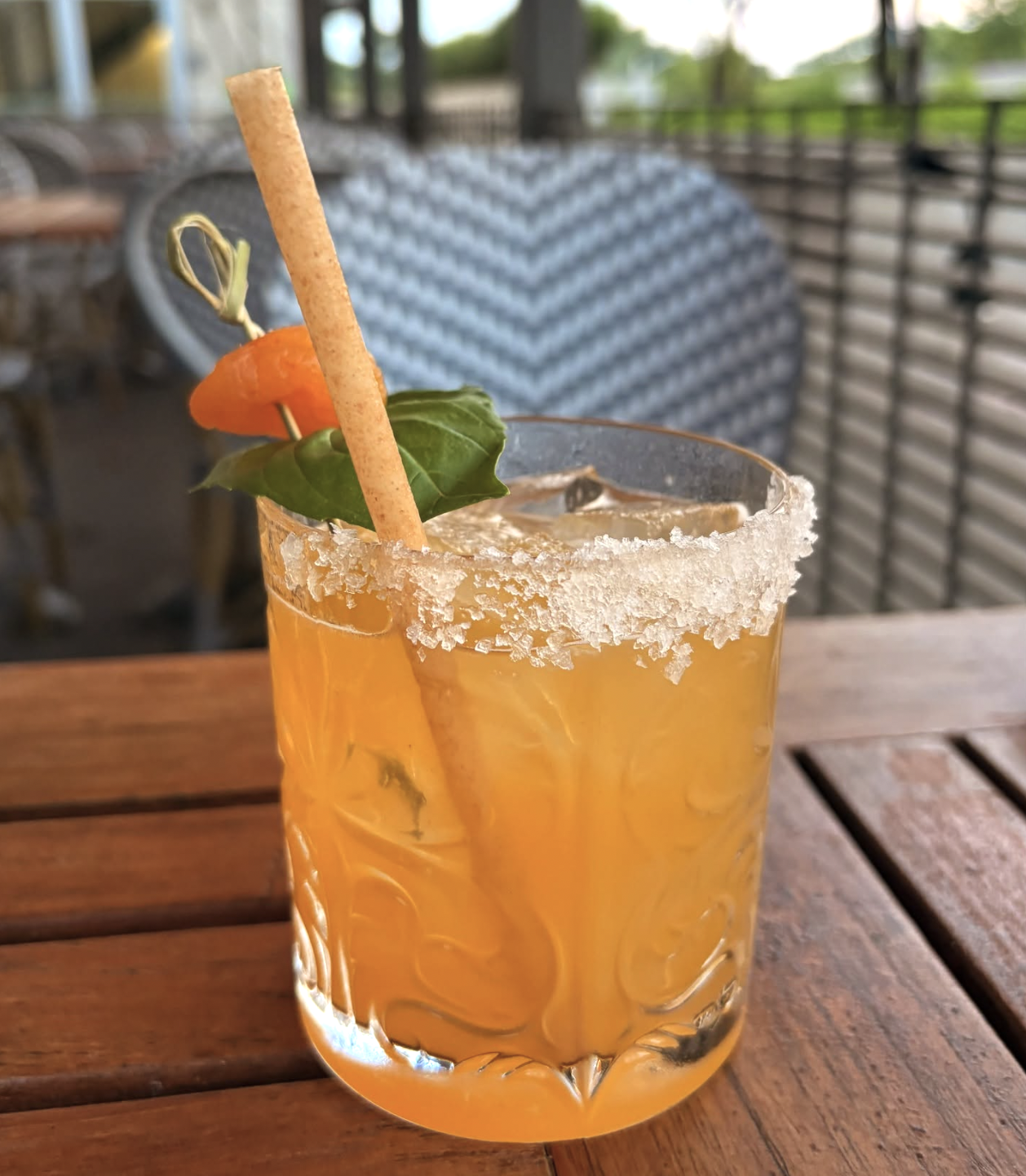 Orange drink in crystal-rimmed glass with carrot, basil, and a straw.