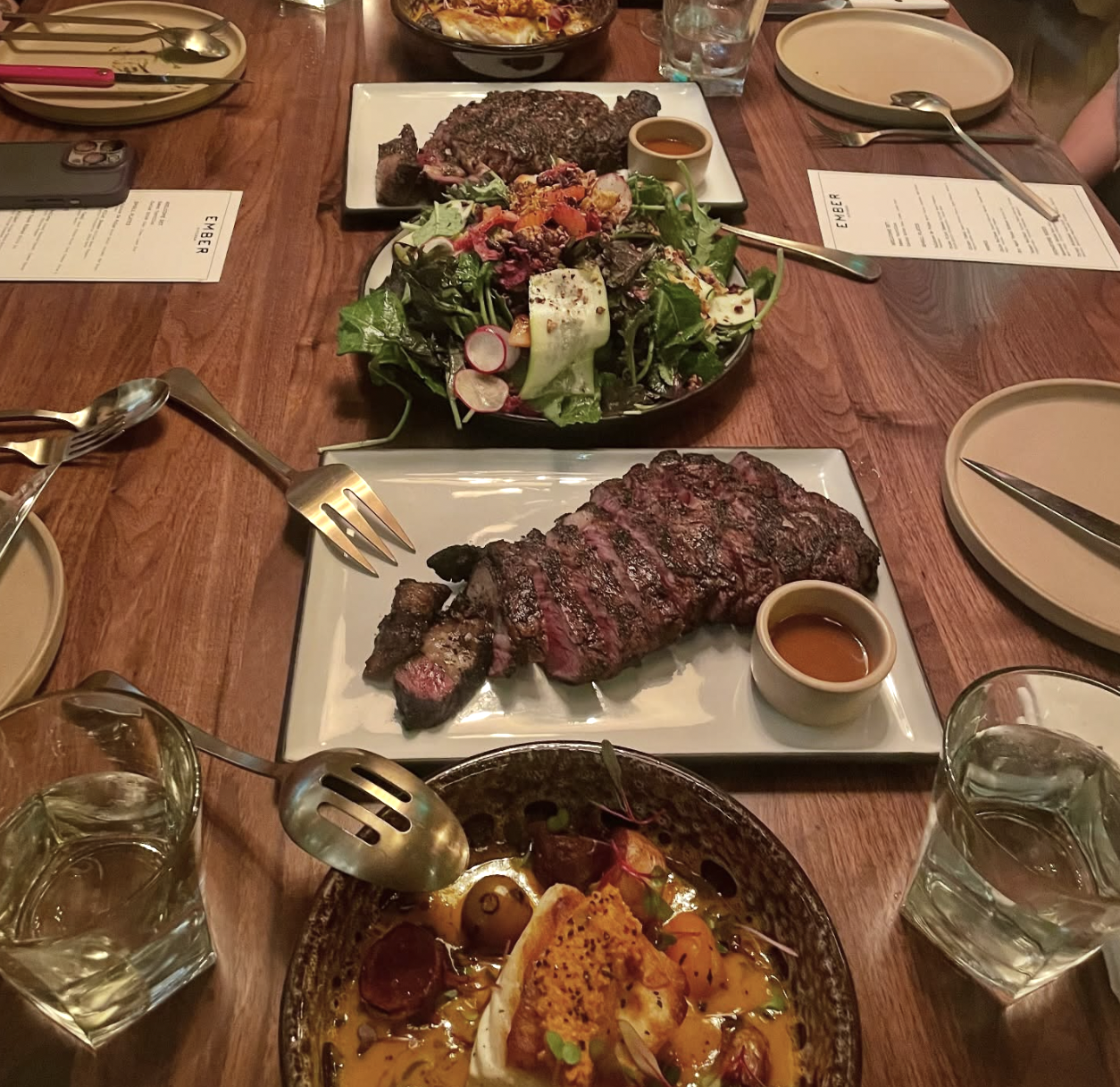 Restaurant table with multiple plates of steak, salad, and sides.