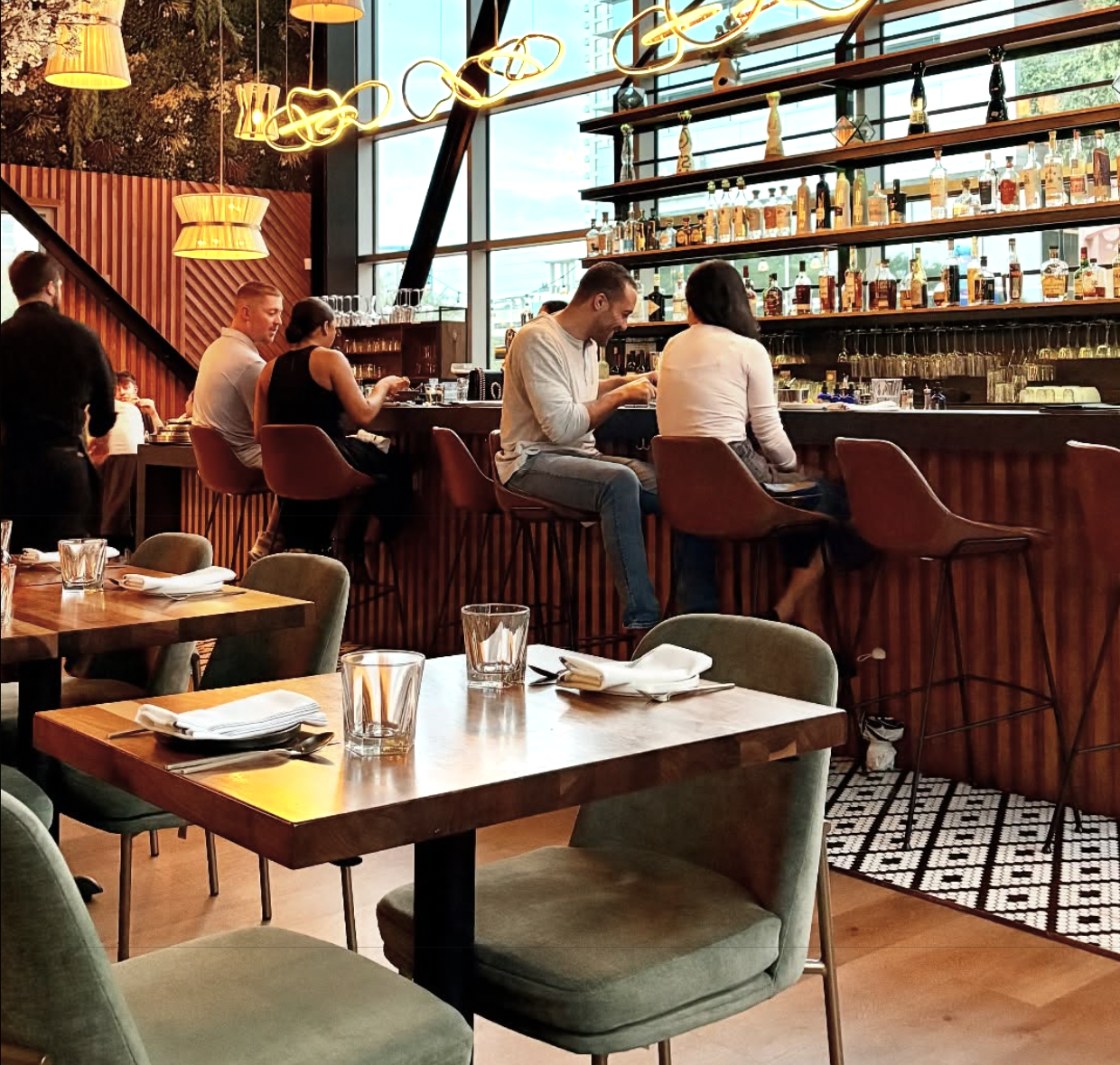 Customers seated at a bar in a modern restaurant, dining tables in foreground.