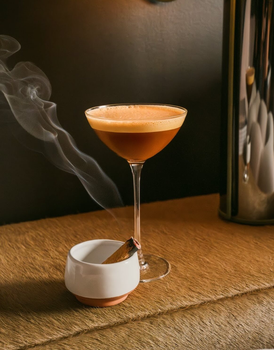 Cocktail glass and smoking palo santo stick on a furry surface.