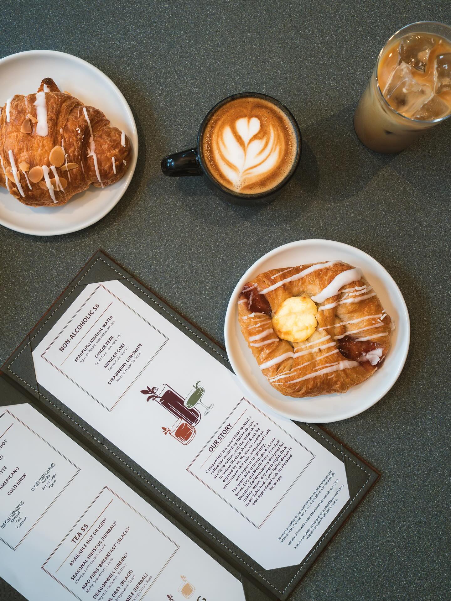Overhead view of croissants, coffees, and a menu on a dark table.