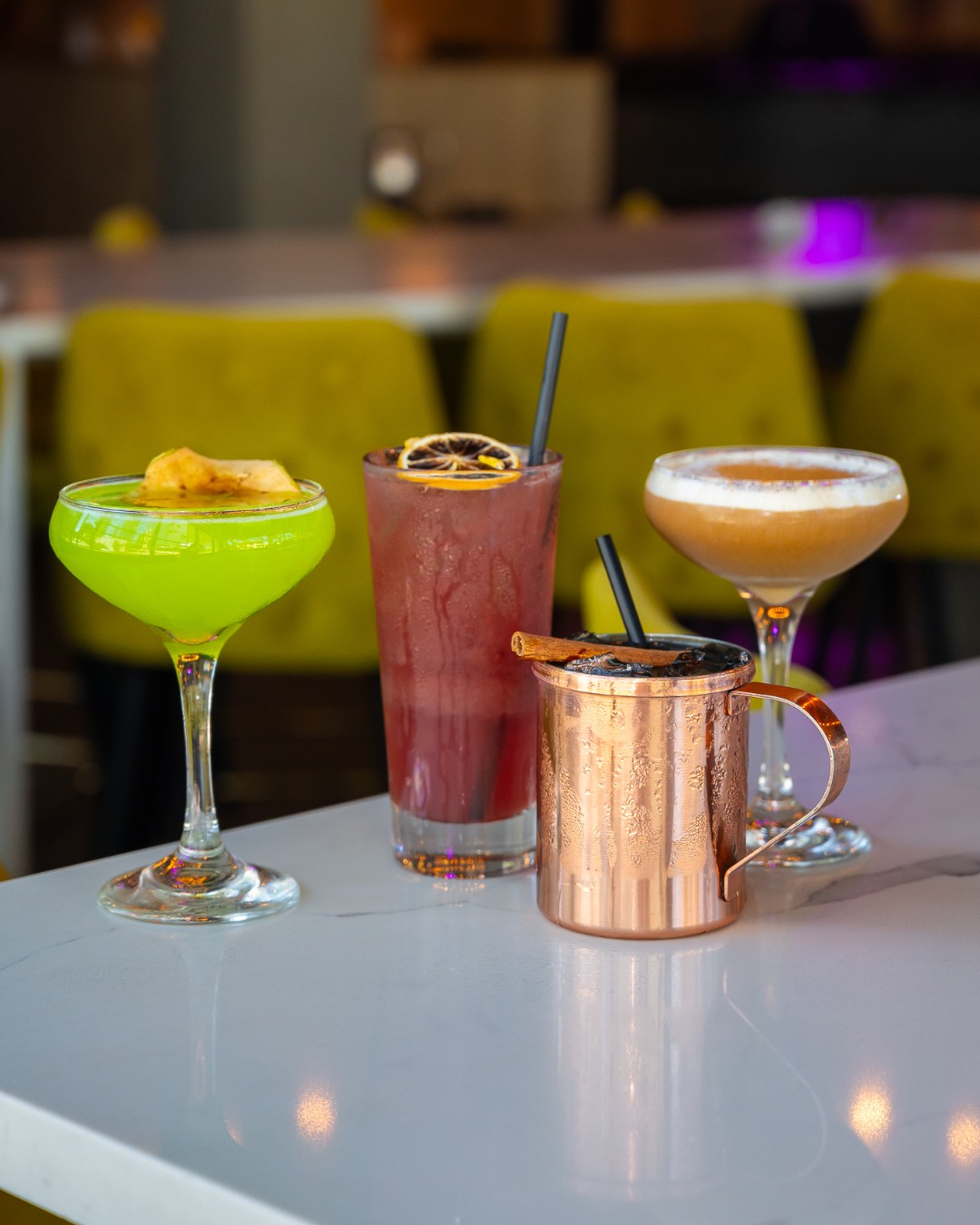 Four drinks in varied glassware and copper mug on a white counter.