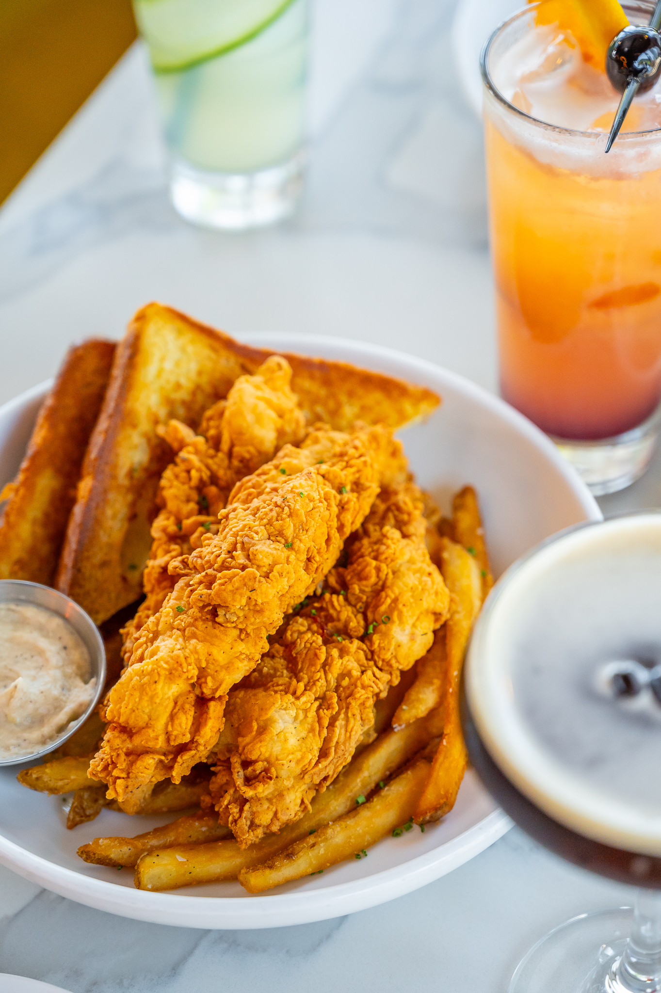 Golden fried chicken tenders, french fries, toast, and three drinks.