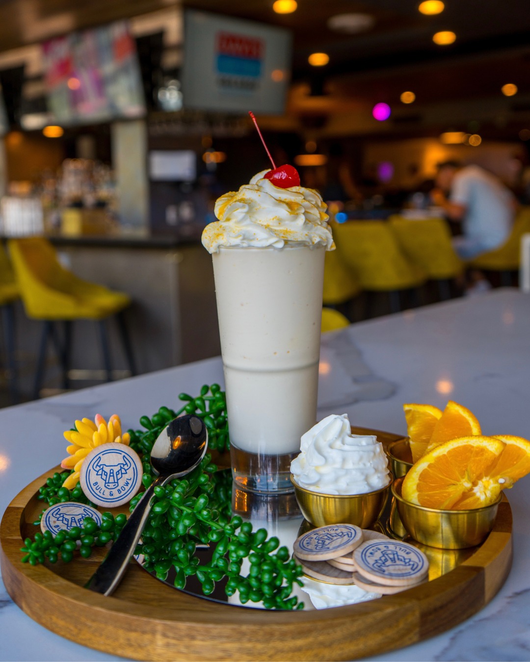 Creamy beverage with whipped cream, cherry, oranges, on a wooden tray.