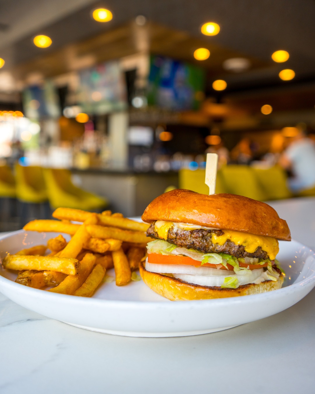 A cheeseburger and fries on a white plate in a restaurant.