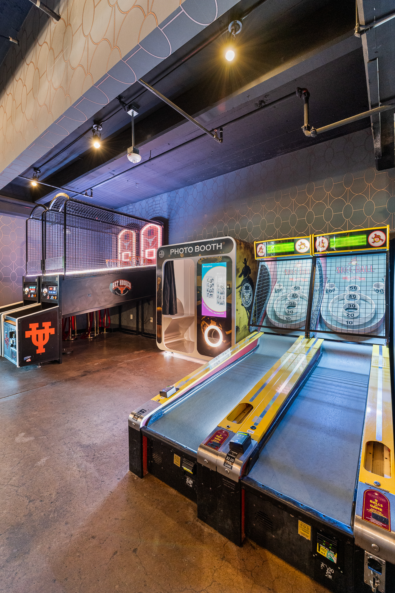 Neon-lit arcade room with Skee-Ball, basketball game, and photo booth.